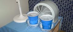 three blue cups sitting on top of a table next to an air conditioner and fan