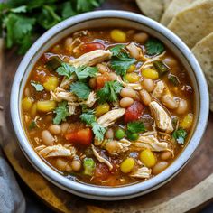 a white bowl filled with chicken and bean soup next to some pita bread on a cutting board