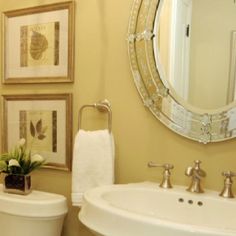 a white toilet sitting next to a bathroom sink under a round mirror and framed pictures on the wall