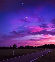 a purple and blue sky with the moon in the distance, as seen from an empty road