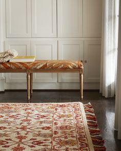 a bench sitting in the middle of a living room next to a white cabinet and window