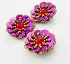 two purple and red flower shaped buttons on a white surface with gold trimmings