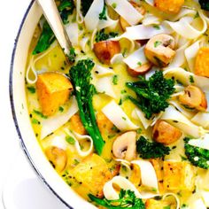 a white bowl filled with pasta, broccoli and other vegetables next to a wooden spoon