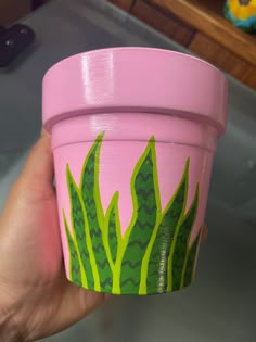 a hand holding a pink cup with green plants painted on the outside and inside it