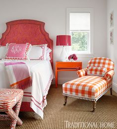 a bedroom with an orange and white checkered bed spread, chair, ottoman and window