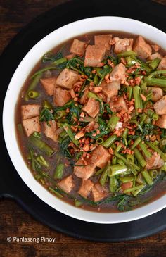 a bowl filled with meat and vegetables on top of a wooden table next to a spoon