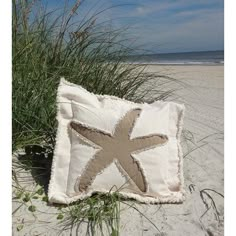 a starfish pillow sitting on top of a sandy beach next to tall green grass