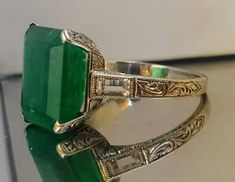 an emerald and diamond ring sitting on top of a glass table next to a white wall