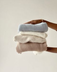 a woman's hand is holding three sweaters in different colors and sizes, all stacked on top of each other