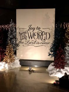 a sign that says joy to the world and some trees in front of it with lights