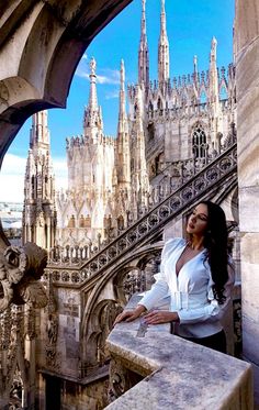 a beautiful woman standing on top of a balcony next to a building with spires