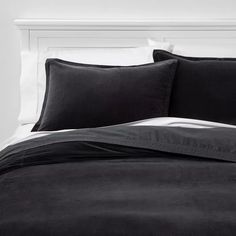 a bed with black sheets and pillows in a white walled room, next to a headboard