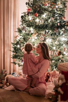 a woman and her child sitting in front of a christmas tree