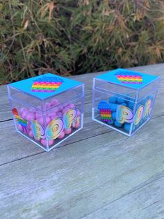 two clear plastic boxes filled with pink and blue candies sitting on a wooden table