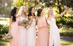 a group of women standing next to each other in front of trees and bushes with one woman taking a selfie