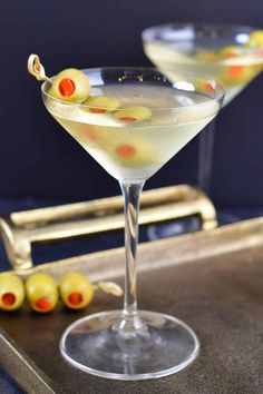 two martini glasses with olives on the rim and one glass filled with white wine