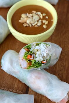 some food is wrapped in paper on a wooden table with a bowl of soup behind it