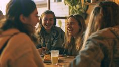 four women sitting at a table laughing and having drinks in a restaurant or bar,