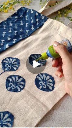 someone is painting the fabric with blue and white designs on it, while another person holds a green marker in their left hand