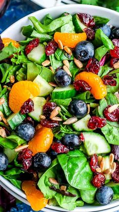 a salad with oranges, blueberries and spinach in a white bowl on a table