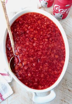 a white bowl filled with red food next to two coke colas on a table