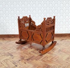 a wooden rocking cradle with intricate carvings on the top and sides, sitting on a hard wood floor