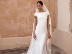 a woman in a white wedding dress with a veil on her head standing next to a wall