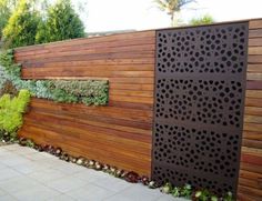 a wooden fence that has plants growing on it and is next to a sidewalk in front of the fence