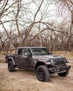 a black jeep parked in the middle of a dirt field next to some bare trees