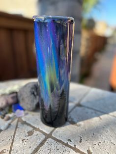 a tall glass sitting on top of a stone table next to a rock and tree