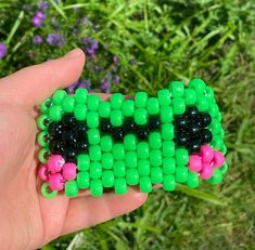 a hand holding a green and pink beaded object