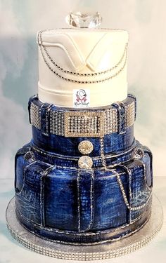 a three tiered blue and white wedding cake on a platter with chain around the edges