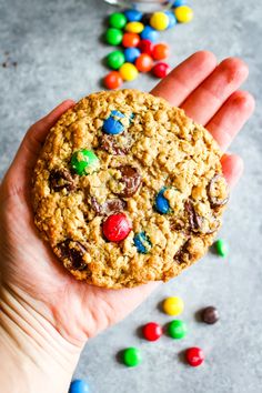 a hand holding a cookie with m & m's on it and candy in the background