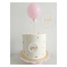 a white cake with polka dots and a pink balloon on top that says g e