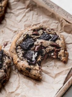 two cookies with chocolate chips and oreos cut in half on top of parchment paper