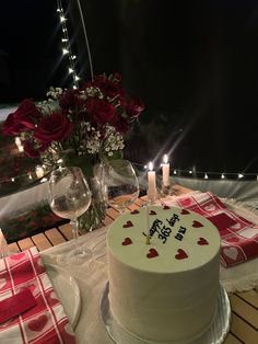 a white cake sitting on top of a table next to two wine glasses and flowers