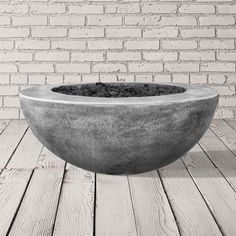 a concrete bowl sitting on top of a wooden table next to a brick wall and floor