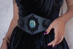 a woman in a black dress is holding onto a belt with an intricate design on it