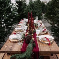 a long wooden table topped with plates covered in pine cones and red ribbon tied to it