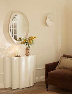 a living room with a chair, mirror and flowers on the table in front of it