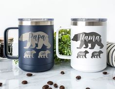 two coffee mugs sitting on top of a counter next to some coffee beans and plants