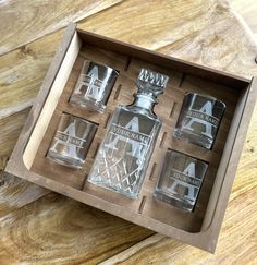 four shot glasses in a wooden box on a table with an empty bottle next to them