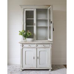 an old white china cabinet with flowers in the bottom drawer and glass doors on top