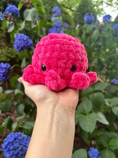 a hand holding a pink crocheted stuffed animal in front of some blue flowers