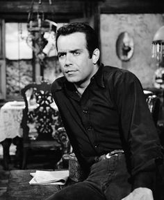 black and white photo of man sitting at table in room with chandelier hanging from ceiling