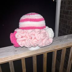 a pink and white crocheted hat sitting on top of a wooden fence next to a brick wall