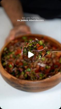 a wooden bowl filled with lots of food on top of a white countertop next to a person's hand