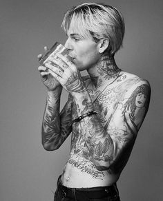 a man with tattoos is drinking from a glass in front of his face and chest