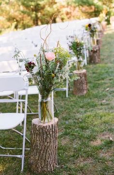 an outdoor ceremony with white chairs and flowers in vases on the side of a tree stump