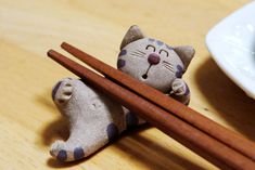 a cat figurine with chopsticks next to it on a wooden table